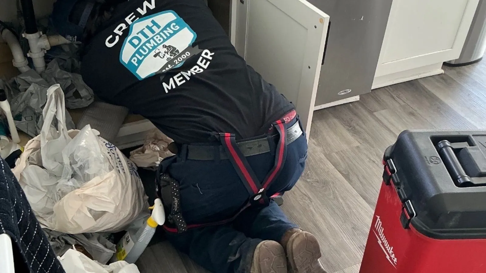 Plumbing technician performing drain cleaning under kitchen area in Burbank home